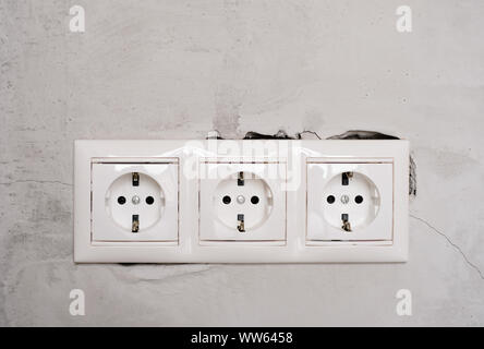 Electric EU socket outlet on gray concrete wall background. Repair in an apartment or in office, replacement of electrical wiring. Close up view. Stock Photo