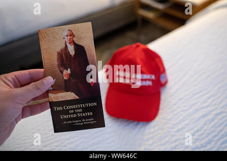 Wenatchee, Washington - July 4, 2019: Hand holds up the Constitution of the United States booklet, with a Make America Great Again hat blurred in back Stock Photo