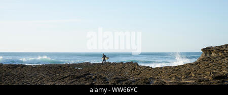 Man carrying surfboard above rock in the waves by the sea Stock Photo