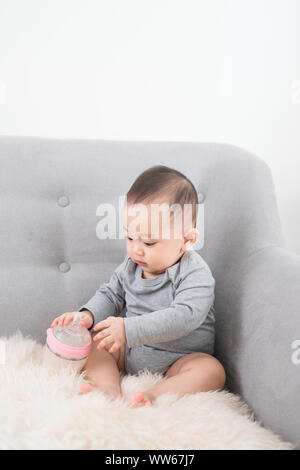 Little cute baby girl sitting in room on sofa drinking milk from bottle and smiling. Happy infant. Family people indoor Interior concepts. Childhood b Stock Photo