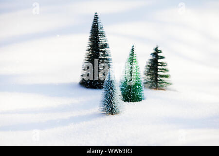 Close view of four tiny fluffy artificial fir trees standing on a white untouched snow. Saving nature concept Stock Photo