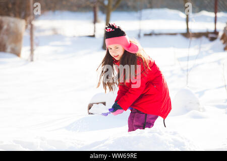 Portrait of cheerful girl busy with snow shoveling. Lovely girl in bright red coat helping her family to clean the road from snow after night snow sto Stock Photo