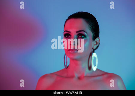 Surprised Woman Pin up Girl. Make up and Beauty Woman over blue background. Neon light on her face with gold sparkle makeup and geometry earrings Stock Photo