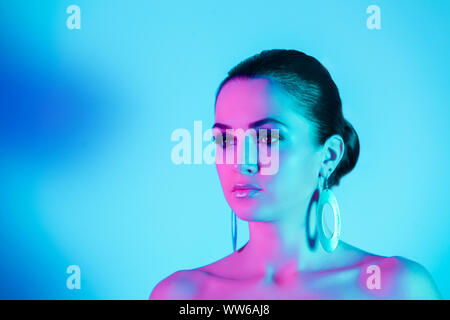 Make up and Beauty Woman over blue background. Neon pink light on her face with gold sparkle makeup Stock Photo