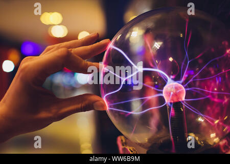 Hand touching a plasma ball with smooth magenta-blue flames. Stock Photo