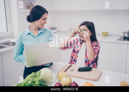 Portrait of two nice cute lovely attractive sweet adorable cheerful people girl fooling closing covering eyes with fresh cucumber pieces in light Stock Photo