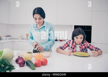 Portrait of two nice cute lovely attractive irritated annoyed bored tired evil girl demanding meal dish mature sweet mom making lunch in light white Stock Photo