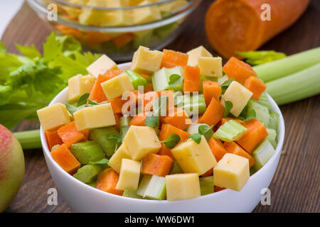 Vitamin salad of celery stalks, carrots, apples and cheese. Vegetable salad with cheese cut into cubes in a plate and a number of ingredients are. Stock Photo