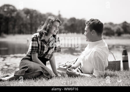 1940s SMILING YOUNG COUPLE MAN AND WOMAN SITTING LYING ON GRASS BY POND LOOKING AT EACH OTHER ENJOYING A PICNIC LUNCH  - c3414 HAR001 HARS NOSTALGIA OLD FASHION 1 COMMUNICATION YOUNG ADULT BALANCE POND TEAMWORK STRONG RELAXING PLEASED JOY LIFESTYLE FEMALES MARRIED RURAL SPOUSE HUSBANDS HEALTHINESS COPY SPACE FRIENDSHIP FULL-LENGTH HALF-LENGTH LADIES PHYSICAL FITNESS PERSONS INSPIRATION CARING MALES B&W PARTNER DATING WIDE ANGLE DREAMS HAPPINESS CHEERFUL LEISURE STRENGTH AND CHOICE ENJOYING EXCITEMENT RECREATION A AT BY ON ATTRACTION SMILES CONNECTION COURTSHIP CONCEPTUAL ESCAPE JOYFUL STYLISH Stock Photo