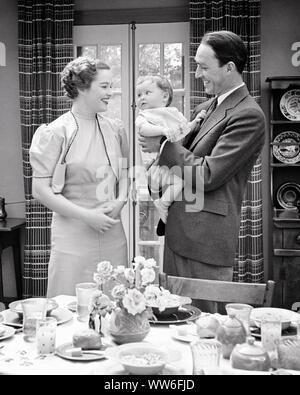 1930s 1940s SMILING WOMAN MOTHER WATCHING MAN FATHER HOLDING BABY SON STANDING AT HOME BESIDE EARLY MORNING BREAKFAST TABLE - d2793 HAR001 HARS BABIES BREAKFAST CLOTHING INDOORS NOSTALGIC PAIR BEAUTY SUBURBAN URBAN OLD TIME BUSY NOSTALGIA OLD FASHION 1 JUVENILE STYLE BALANCE TEAMWORK INFANT STRONG SONS PLEASED JOY LIFESTYLE FEMALES MARRIED SPOUSE HUSBANDS HEALTHINESS HOME LIFE COPY SPACE FULL-LENGTH HALF-LENGTH LADIES PERSONS CARING MALES B&W MORNING PARTNER SUCCESS SUIT AND TIE HAPPINESS WELLNESS CHEERFUL EARLY PROTECTION STRENGTH PRIDE AT AUTHORITY SMILES CONCEPTUAL BESIDE JOYFUL STYLISH Stock Photo