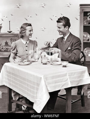 1930s 1940s SMILING MAN AND WOMAN AT BREAKFAST TABLE WOMAN SERVING TOAST MAN WEARING SUIT AND TIE - d112 HAR001 HARS PLEASED JOY LIFESTYLE SATISFACTION FEMALES MARRIED STUDIO SHOT SPOUSE HUSBANDS HEALTHINESS HOME LIFE COPY SPACE FRIENDSHIP HALF-LENGTH LADIES PERSONS TABLECLOTH CARING MALES B&W MORNING PARTNER HOMEMAKER SUIT AND TIE HAPPINESS HOMEMAKERS CHEERFUL TOAST AND PRIDE HOUSEWIVES SMILES CONNECTION DINNERS JOYFUL STYLISH DINING ROOM PERSONAL ATTACHMENT AFFECTION COOPERATION DINE EMOTION NEWLYWEDS TOGETHERNESS WIVES YOUNG ADULT MAN YOUNG ADULT WOMAN BLACK AND WHITE CAUCASIAN ETHNICITY Stock Photo