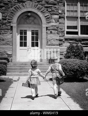 1940s 1950s BOY AND GIRL HOLDING HANDS HOLDING LUNCH BOX AND BOOK BAG WALKING UP SIDEWALK TO FRONT DOORS OF SCHOOL BUILDING - s2390 HAR001 HARS ELEMENTARY FRIEND LIFESTYLE FEMALES BROTHERS UNITED STATES COPY SPACE FRIENDSHIP FULL-LENGTH UNITED STATES OF AMERICA CARING MALES SIBLINGS SISTERS B&W NORTH AMERICA GOALS NORTH AMERICAN SCHOOLS GRADE KINDERGARTEN PRESCHOOL PAIL AND EXTERIOR KNOWLEDGE REAR VIEW OF OPPORTUNITY TO UP PRIMARY SIBLING CONNECTION FRIENDLY PRE-SCHOOL STYLISH K-12 BACK VIEW COOPERATION GRADE SCHOOL GROWTH JUVENILES TOGETHERNESS BLACK AND WHITE BOOK BAG CAUCASIAN ETHNICITY Stock Photo