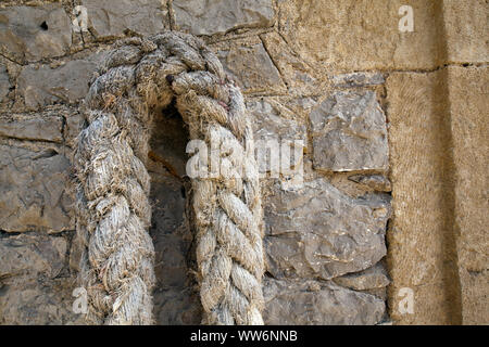 thick hemp rope hangs on quarrystone wall in Greece Stock Photo
