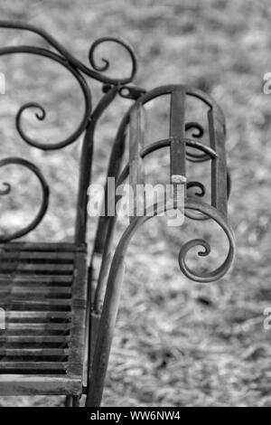 filigree rusty park bench in front of meadow area Stock Photo