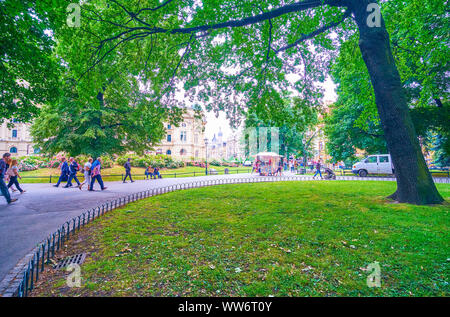 KRAKOW, POLAND - JUNE, 13, 2018: The scenic view on the greenery of the garden surrounding the historical center with busy walking alley through the c Stock Photo