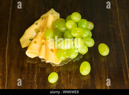 A bunch of grapes and slices of cheese on a wooden background. Stock Photo