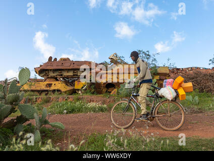 Eritrean man riding a bicycle in front of the military tank graveyard, Central region, Asmara, Eritrea Stock Photo