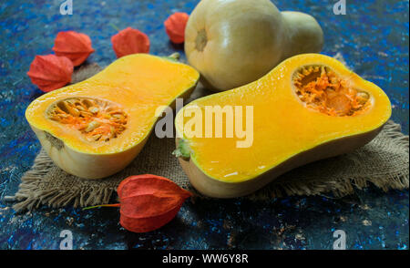 Whole and cut in half pumpkin and physalis flowers on a blue background. Close-up. Autumn holidays concept. Stock Photo