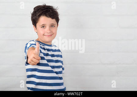 Little boy smiling showing thumb up on brick background Stock Photo