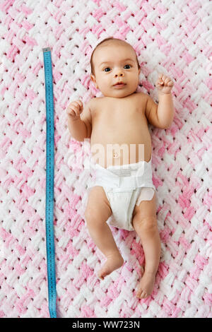 baby girl lying with measure tape on blanket Stock Photo