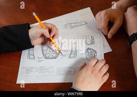 Two people reviewing technical engineering drawings and design plans at a desk. Stock Photo