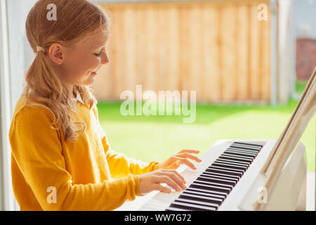 Portrait of pretty little girl having piano lesson at modern white e-piano at home Stock Photo