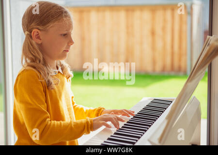 Portrait of pretty little girl having piano lesson at modern white e-piano at home Stock Photo