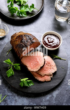 Medium rare roast beef. Sliced grilled beef on wooden board over stone background. Stock Photo