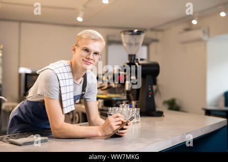 Young confident waiter with notepad and pen reading notes before preparing order Stock Photo