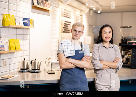 Young successful waiters in uniform looking at you while standing by workplace Stock Photo
