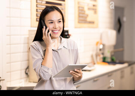 Young cheerful manager of restaurant communicating with client on mobile phone Stock Photo