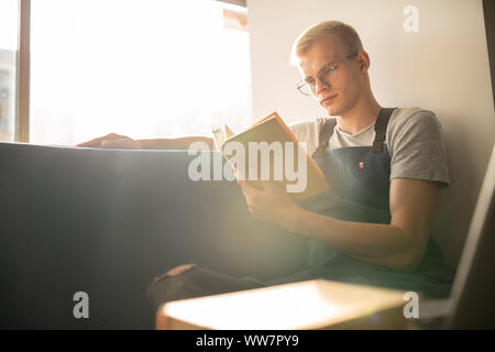 Serious young waitress of cafe or restaurant in workwear looking at book page Stock Photo