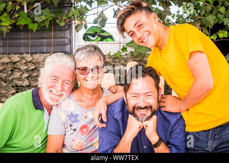 four different mixed generations grandfather father son all together in leisure activity. mobile phones on the table to represent technology and family concept connected to the modern world. colored clothes and happiness Stock Photo