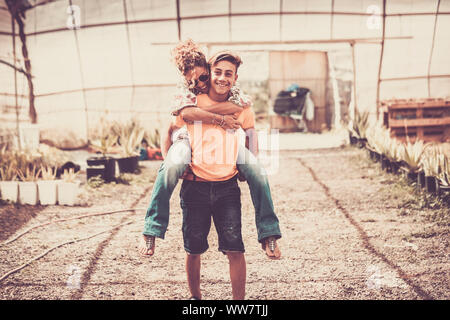 young beautiful teenager play with his mother middle age pretty woman carrying her to his back. couple mother son having fun together like a perfect family in outdoor leisure activity. happy people concept Stock Photo
