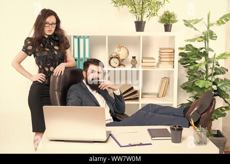 Typical office life. Man bearded hipster boss sit in leather armchair office interior. Boss and secretary girl at workplace. Relations at work. Busine Stock Photo