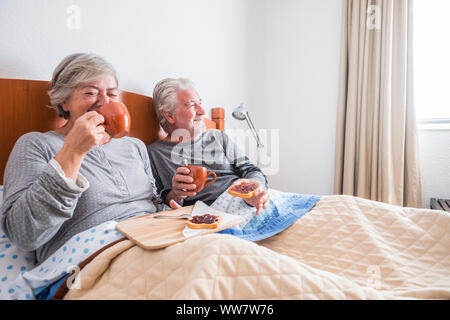 adult people aged couple having fun laughing and smiling on the bed at home. indoor bedroom scene family having brekfast lay down. window light and bright image