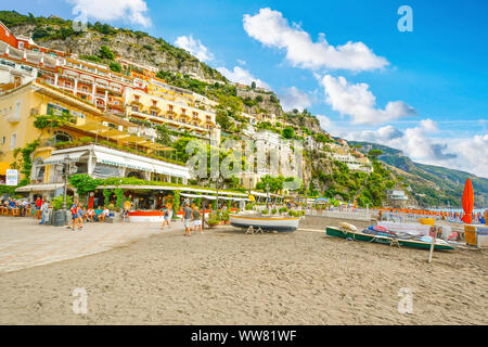 Tourists enjoy the sandy beach, restaurants, resorts and promenade at the coastal hillside city of Positano, Italy on the Amalfi Coast. Stock Photo