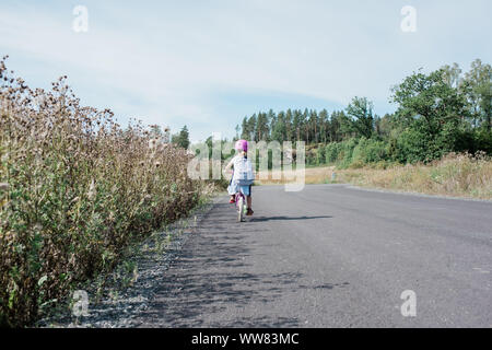 rear view of a young girl cycling home from school along country road Stock Photo