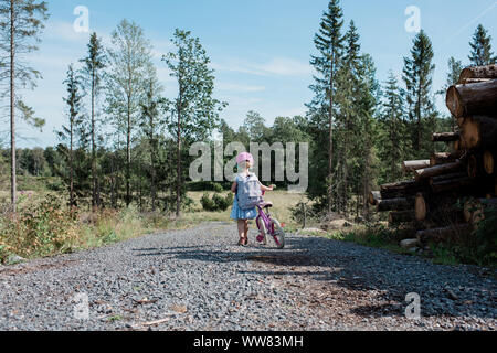 young girl walking home from school with her bike in the countryside Stock Photo