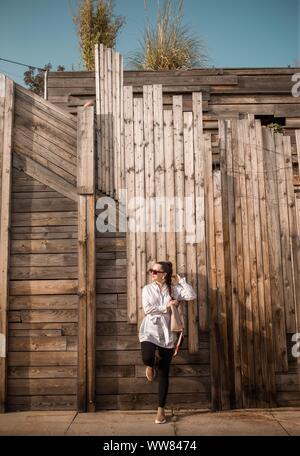 Young woman standing and leaning with one leg on plank wall Stock Photo
