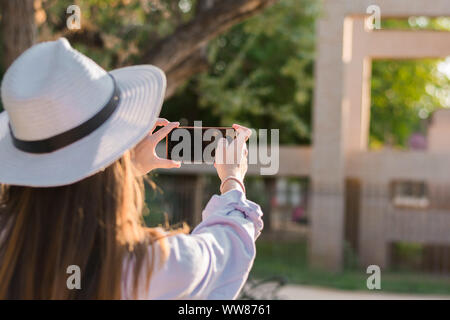 Young woman is taking a picture with her smartphone in a park. Leisure, lifestyle, technology Stock Photo