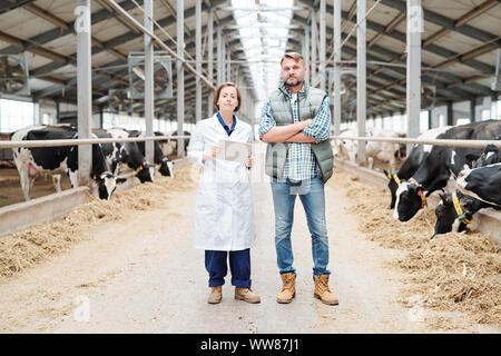 Two young confident farmers in workwear standing in front of camera in aisle