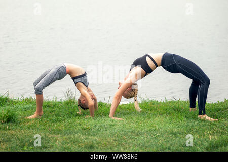 Woman and child are training near the lake at the summer park. Sporty mother and daughter. Fitness, yoga. Stock Photo