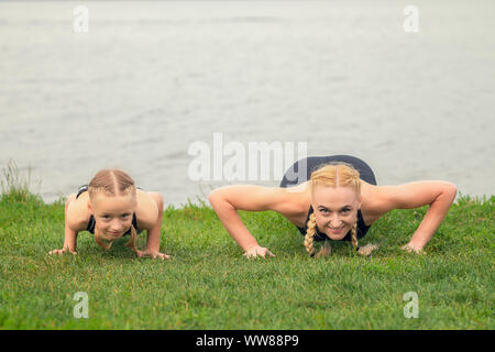 woman and child are training near the lake on the green grass, sporty mother and daughter, fitness, yoga Stock Photo