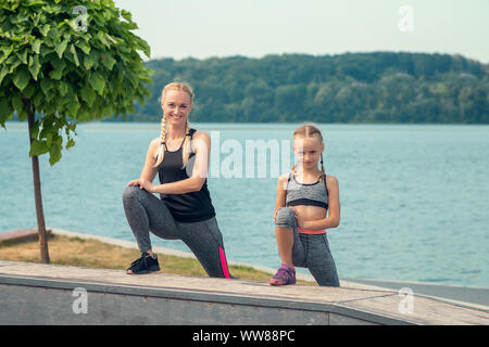 Woman and child are training near the lake at the summer park. Sporty mother and daughter. Fitness, yoga. Stock Photo