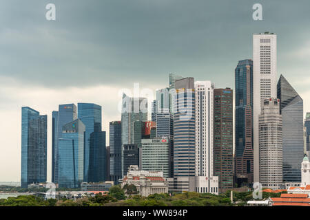 Singapore - March 20, 2019: Line of financial district skyscrapers from the bay to Victoria Theatre clock tower under dark gray cloudscape, with green Stock Photo