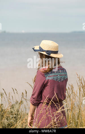 Young woman in summer dress and straw hat at the coast Stock Photo