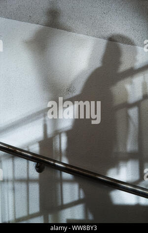 Abstract background of shadows man walking up the stairs and street light on a white wall. Stock Photo