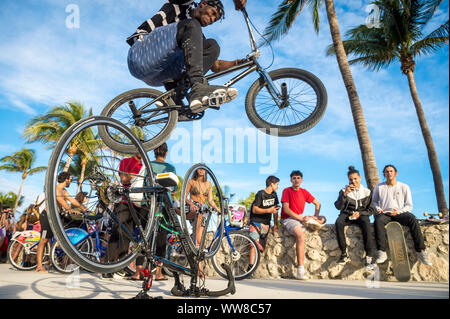 MIAMI - DECEMBER 27, 2017: A young daredevil cyclist performs a stunt jump over another bicycle in front of spectators on the beachfront boardwalk. Stock Photo