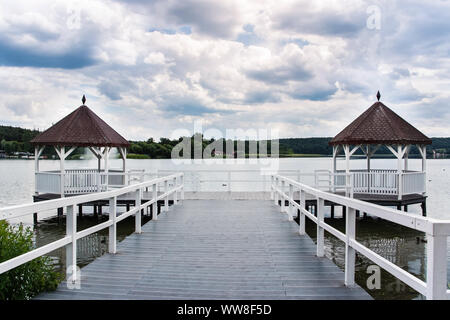 Beautiful white roofed pier with wooden huts on lake, green forest and puffy clouds in background, Barlinek, Poland Stock Photo